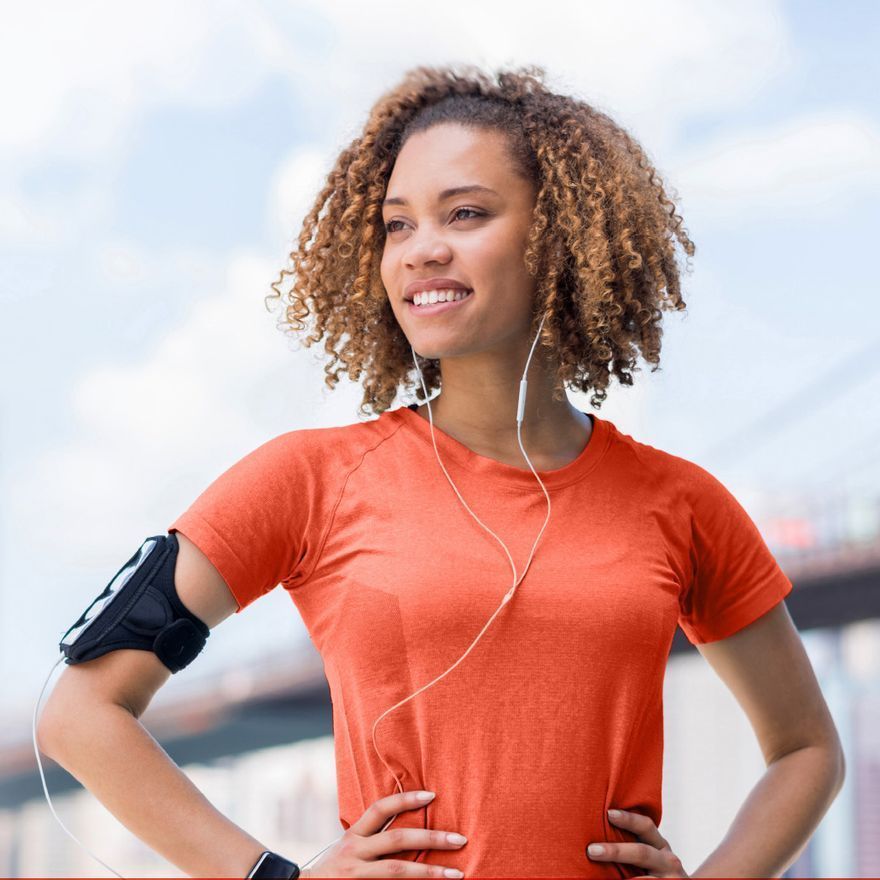 a woman wearing an orange shirt and headphones stands with her hands on her hips