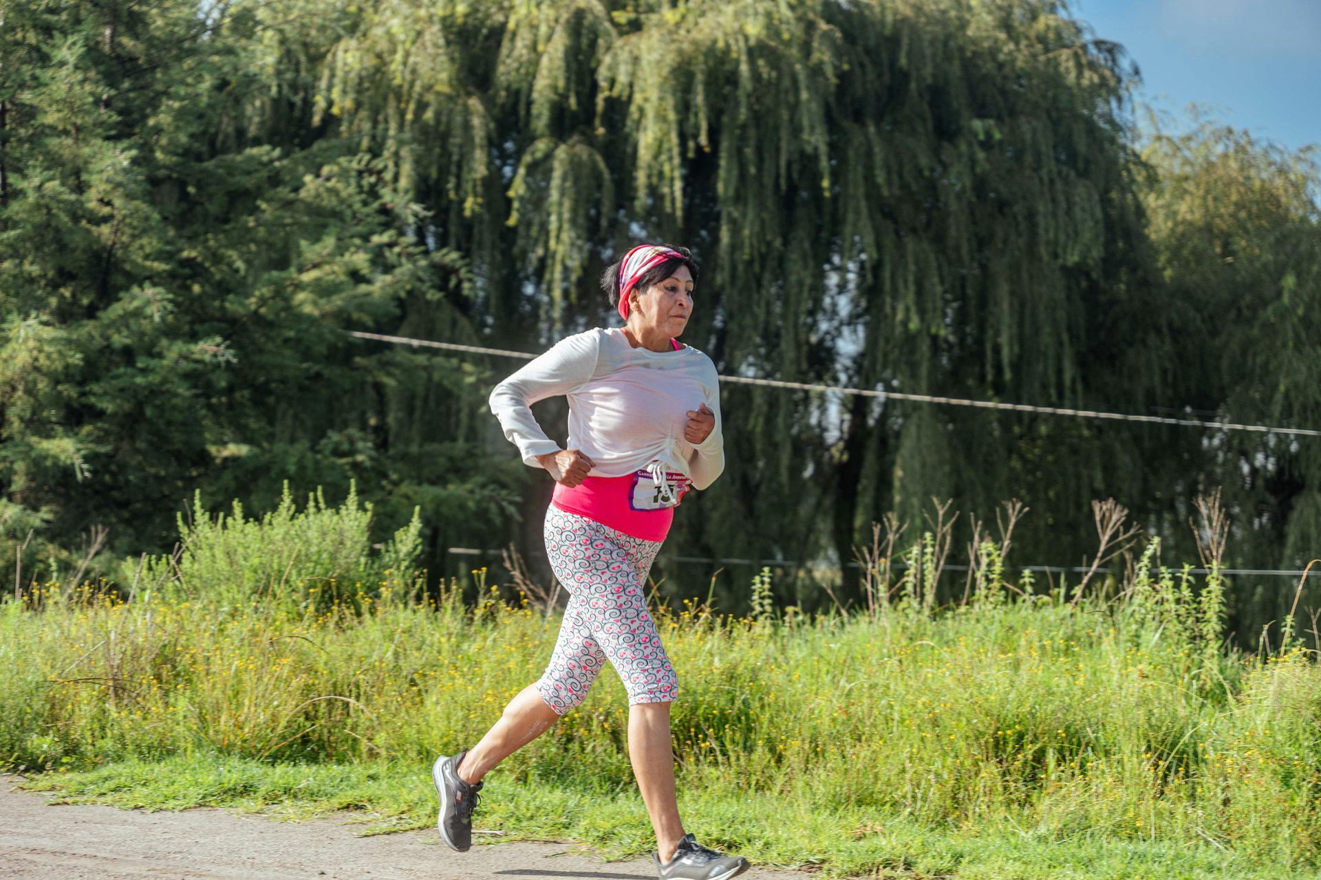 Runner in a pink top and patterned leggings jogging along a grassy path by a lake.