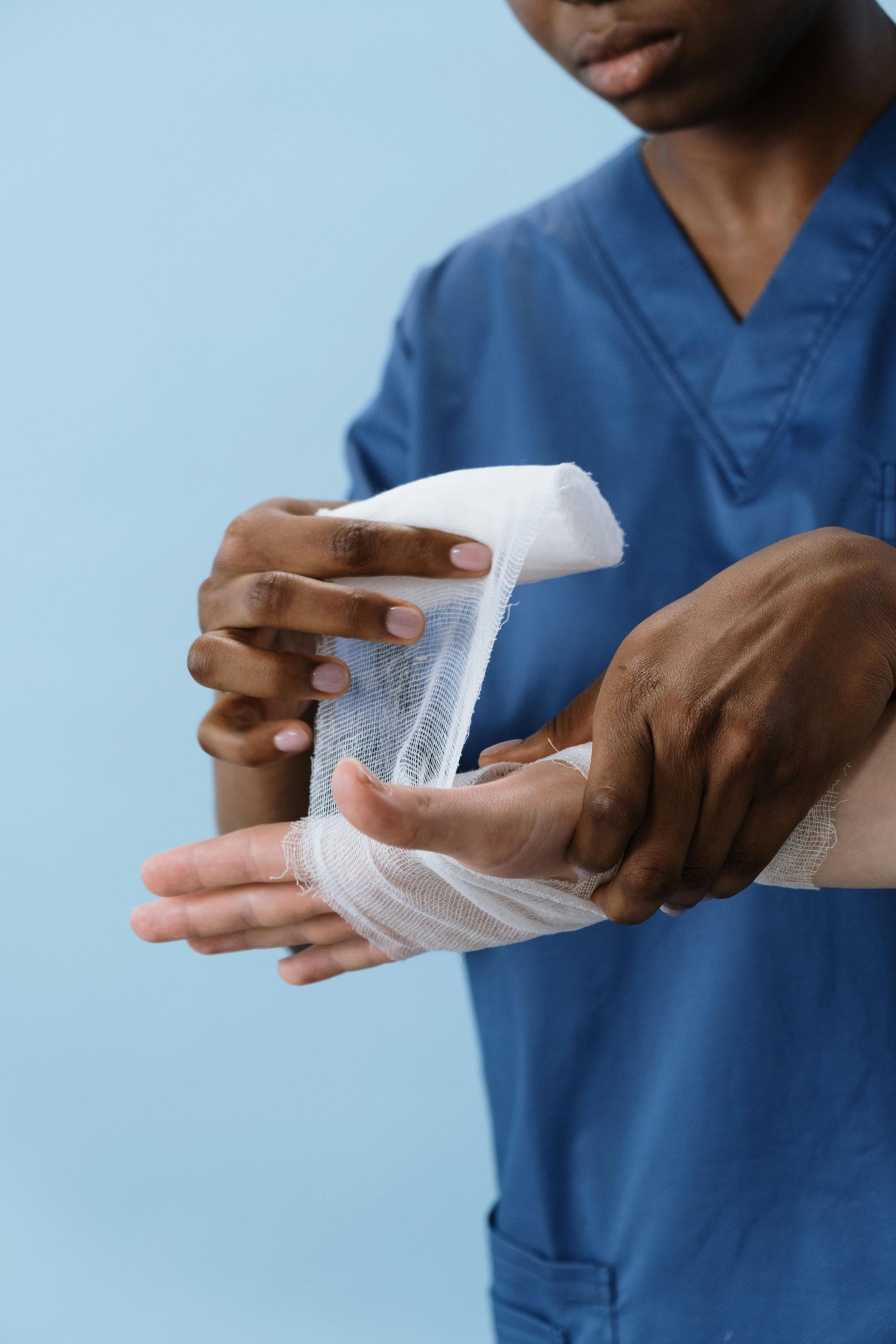 Person wrapping a hand with a white bandage in blue medical scrubs
