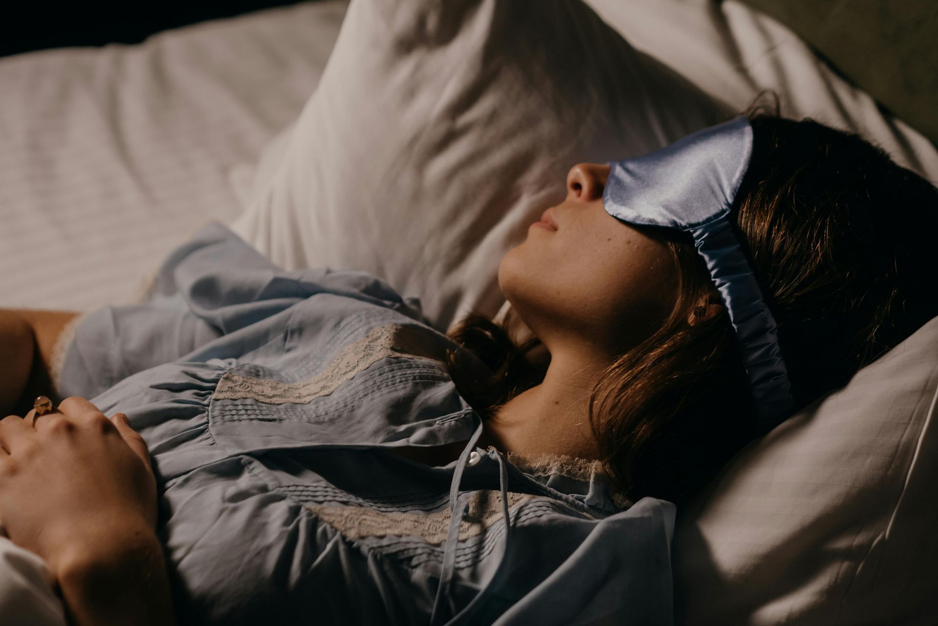 Person lying in bed with an eye mask on, resting under soft warm light