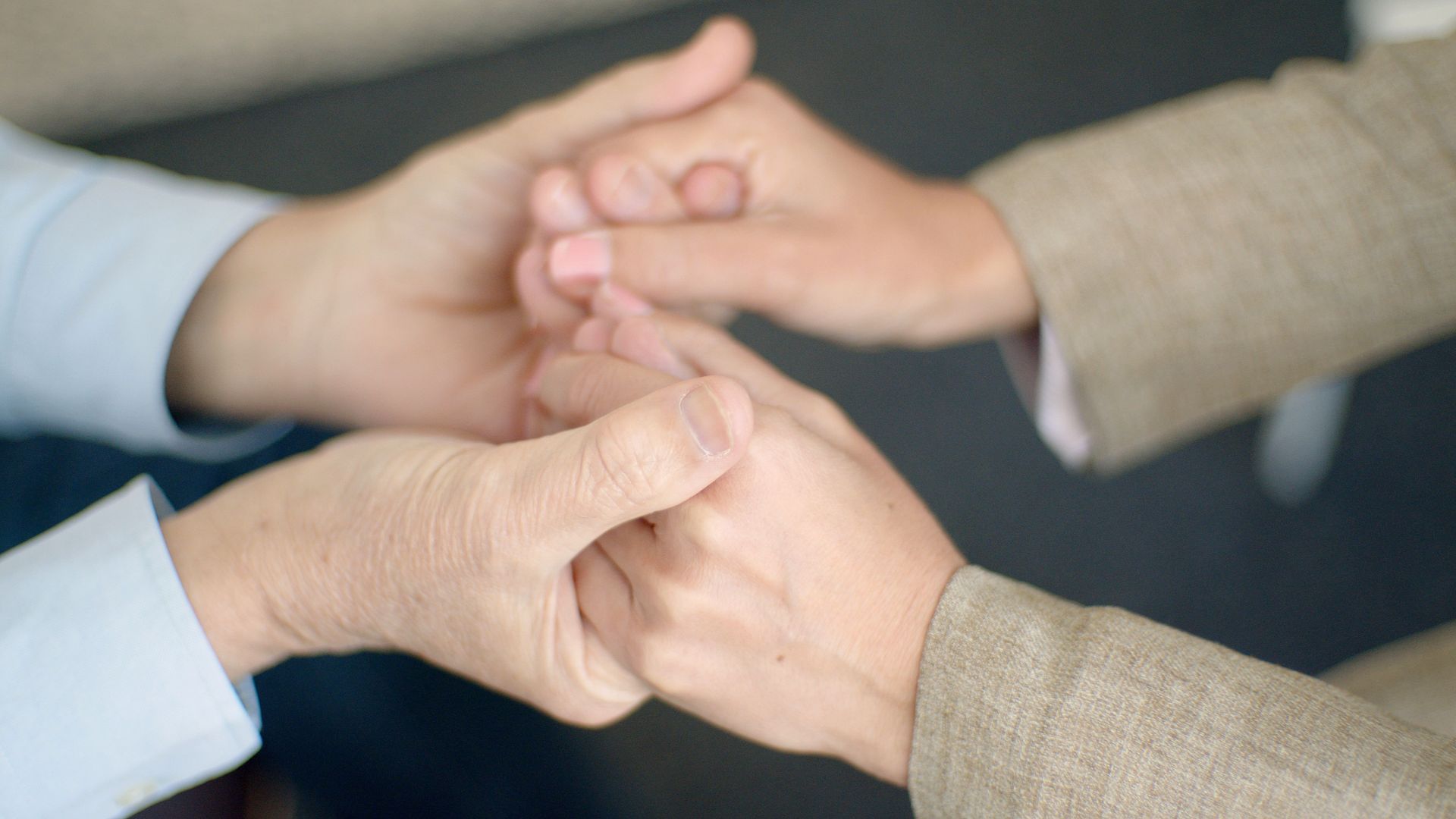Two pairs of hands clasped together in a circle on a plain background