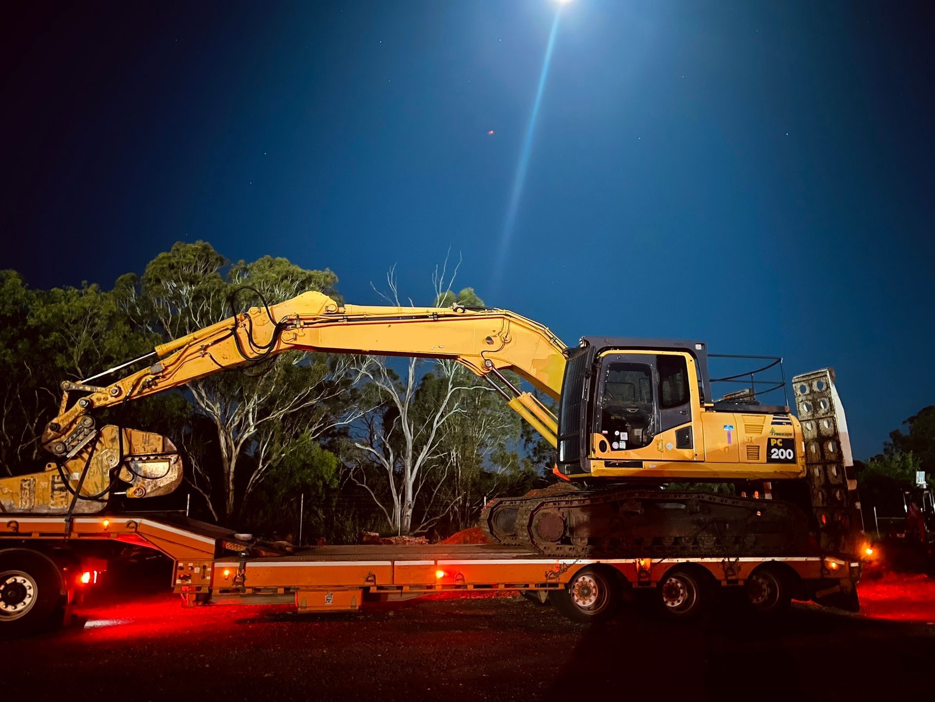 A yellow excavator is sitting on top of a trailer at night.