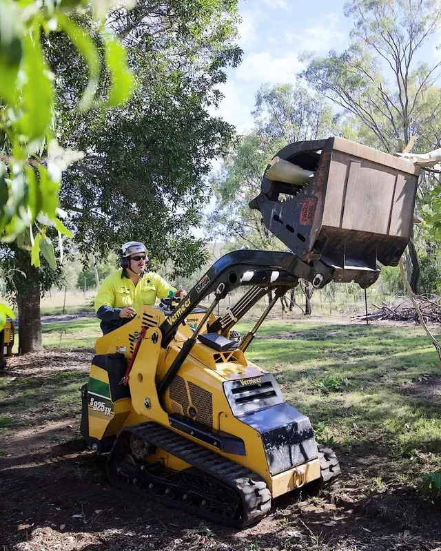 A man is driving a small yellow tractor in a park.