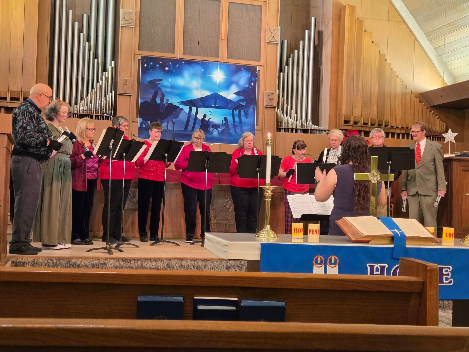 A handbell choir performing in a church. Musicians ring bells while a conductor directs.