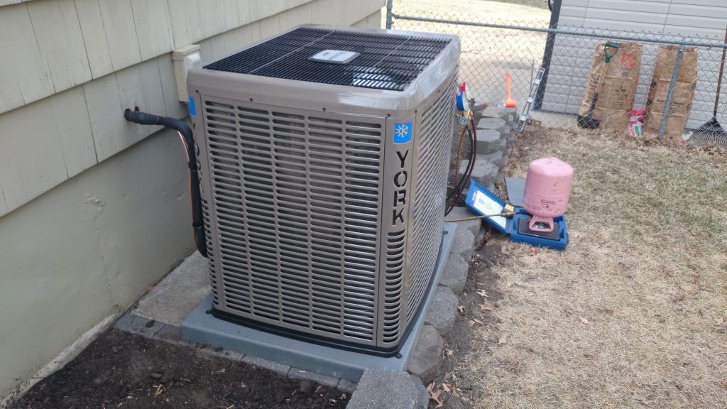 York air conditioner unit beside a house, near a chain link fence.