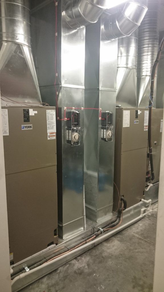 Two beige HVAC units with ductwork in a basement.