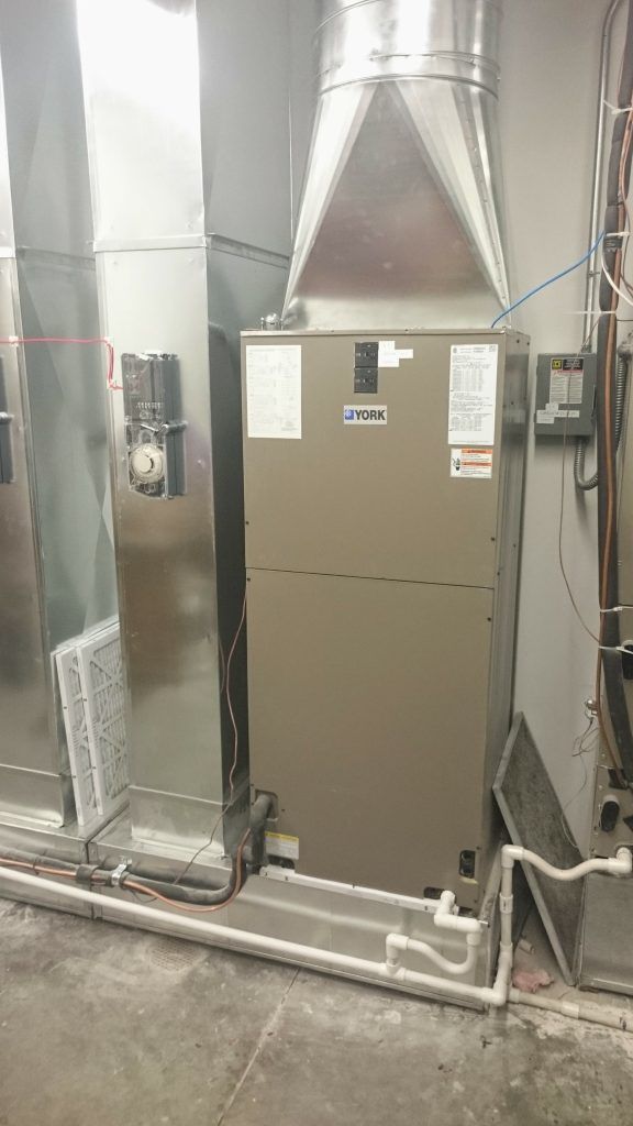 A furnace unit with metal ductwork, filters, and connected pipes in a room.