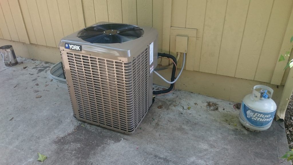 York air conditioner unit next to a house with a propane tank on a concrete slab.