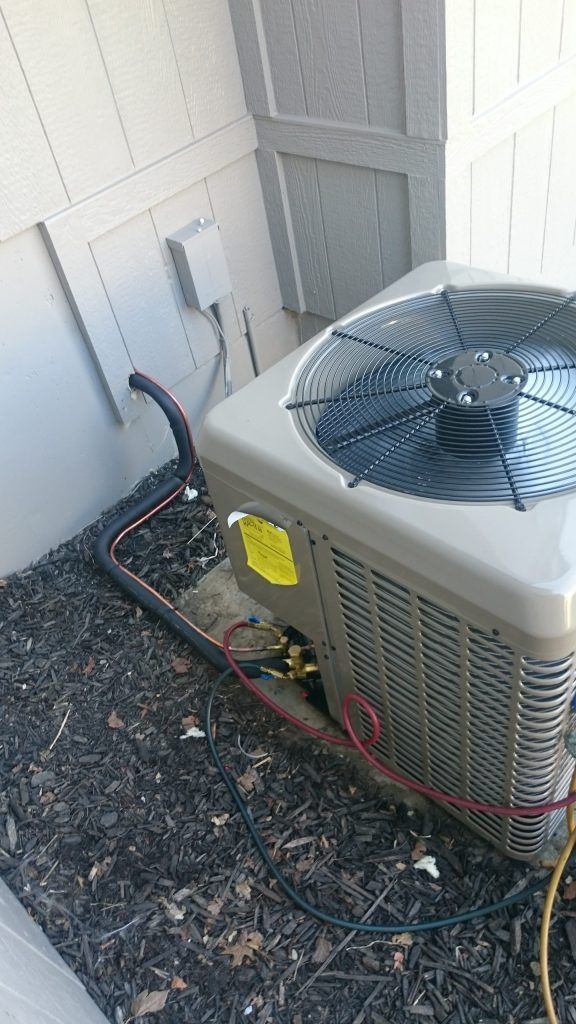 Air conditioner unit outside a building, black tubing, yellow sticker, gray.