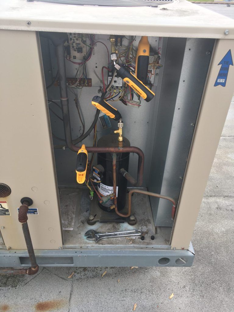 Open air conditioning unit with tools, lights, and a technician's work.