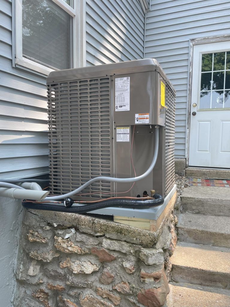 Air conditioning unit next to a building with blue siding and stone steps.
