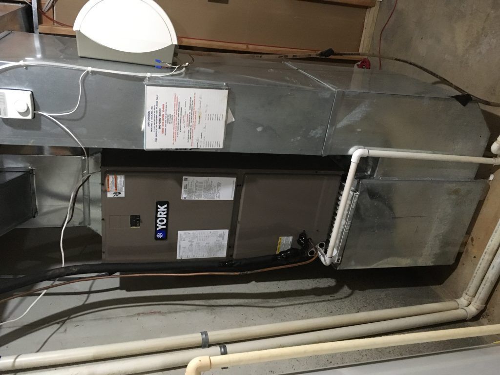 A furnace in a basement, with ductwork and PVC pipes.