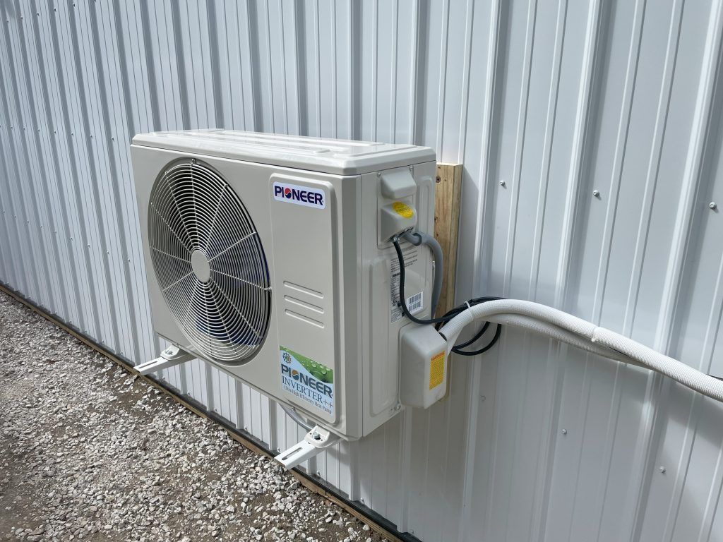 Air conditioner unit mounted on a white corrugated metal wall.