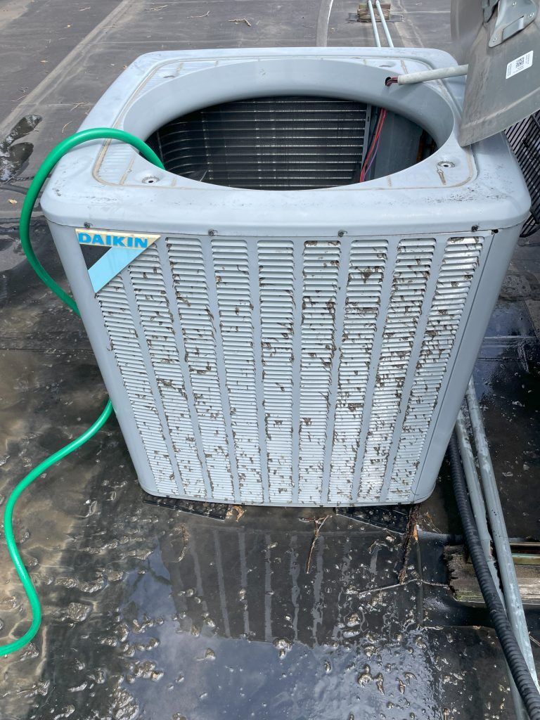 Daikin AC unit on a rooftop, showing its top and front. A green hose is coiled nearby.