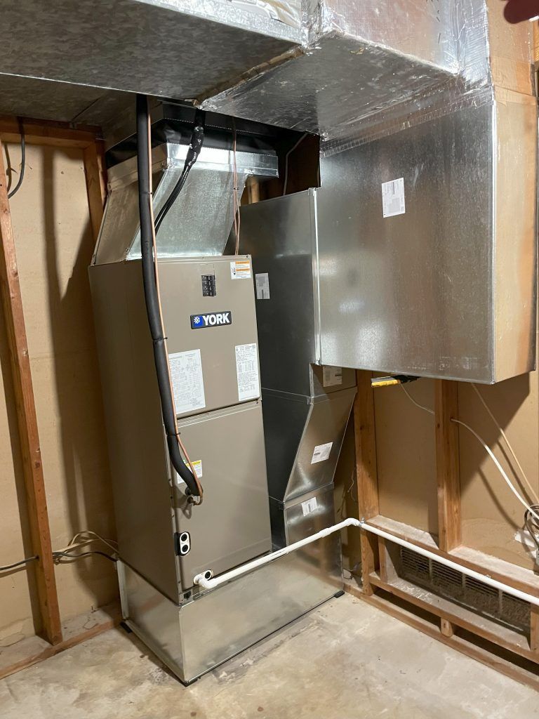 HVAC unit in a basement corner with metal ductwork, pipes, and exposed wooden framing.