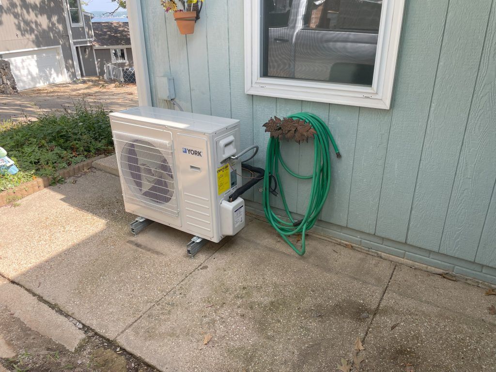 Air conditioner unit on wheels next to house with green hose.