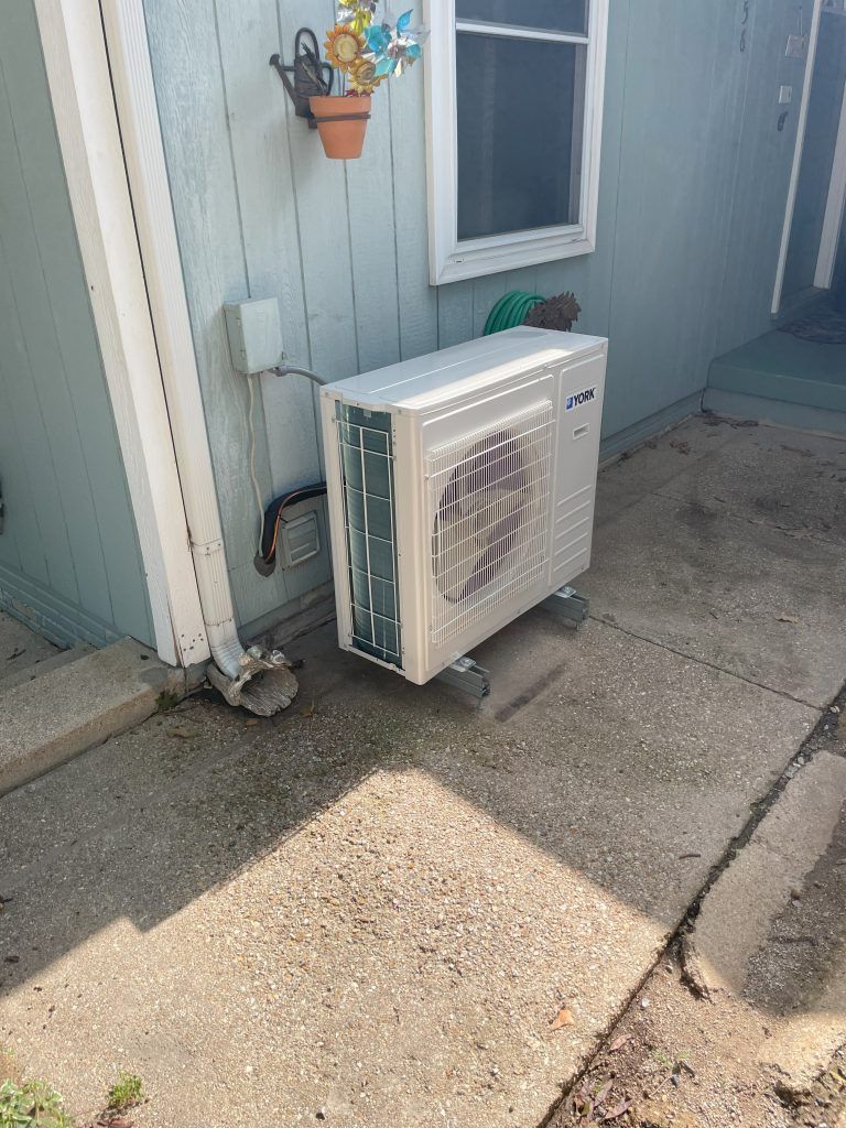 Outside view of a blue house with a white air conditioning unit on wheels, beside a downspout.