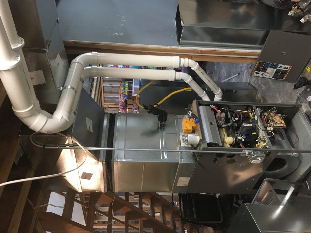 Furnace with white PVC pipes, electrical components, and metal ductwork in an attic setting.