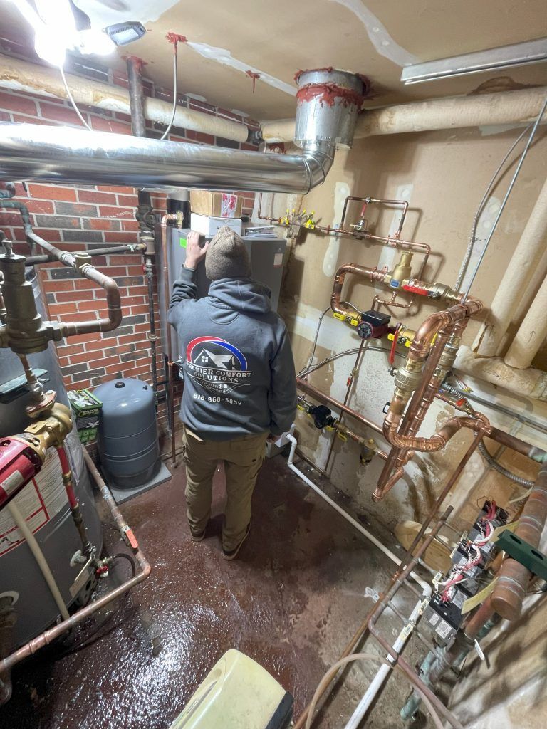Person in a grey hoodie working on complex copper piping in a mechanical room.