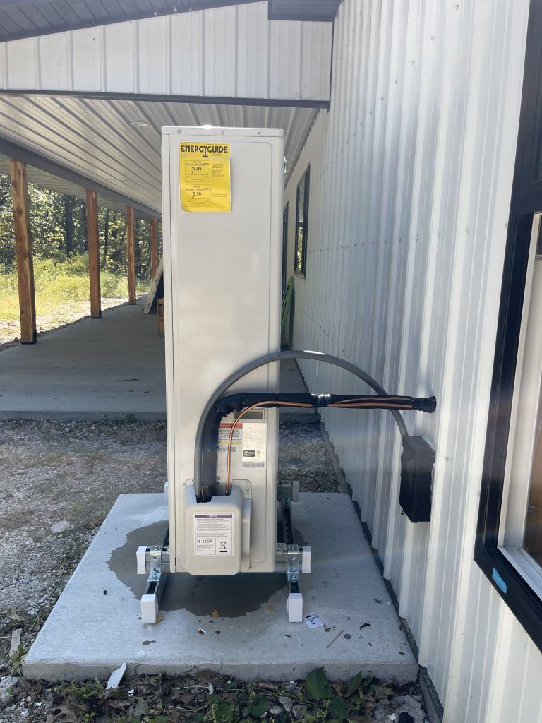 An air conditioning unit on a concrete pad next to a building with a covered patio.