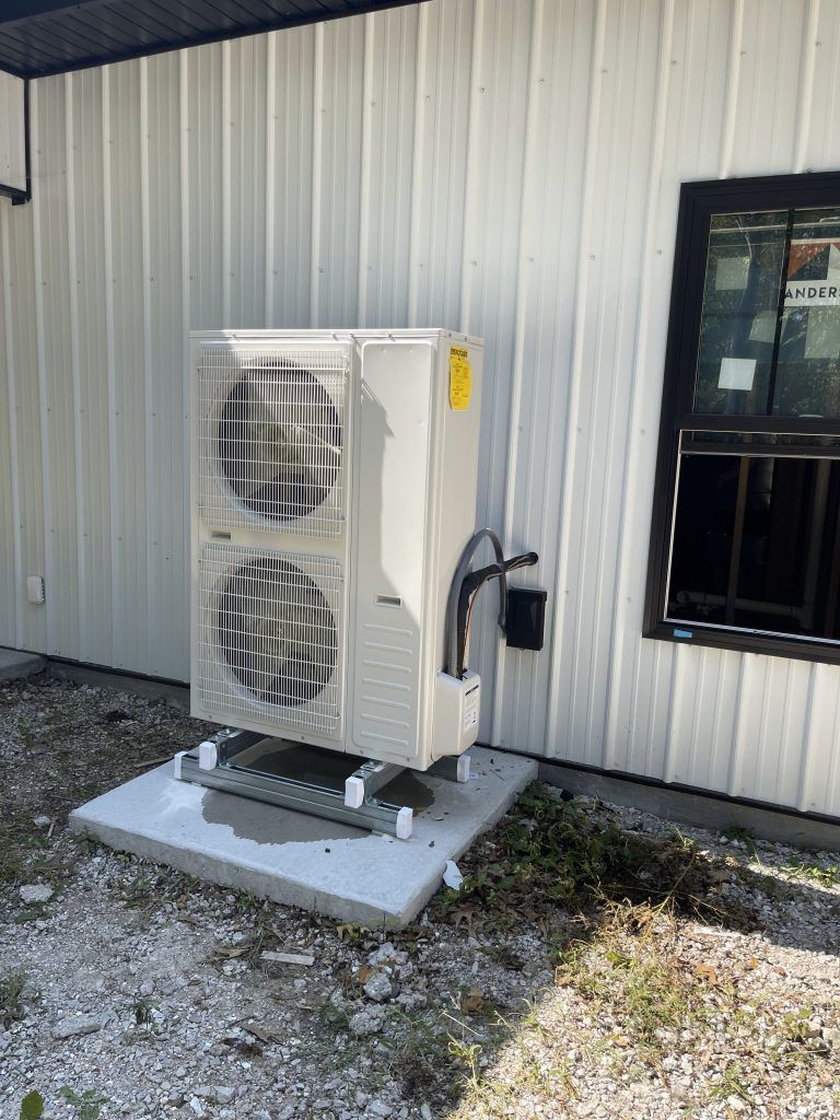 White air conditioning unit outside a building with a black-framed window.