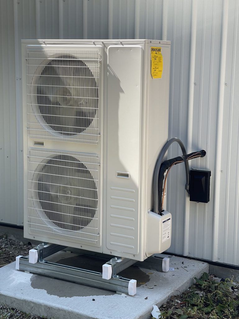 Air conditioning unit mounted on a concrete pad against a white building.