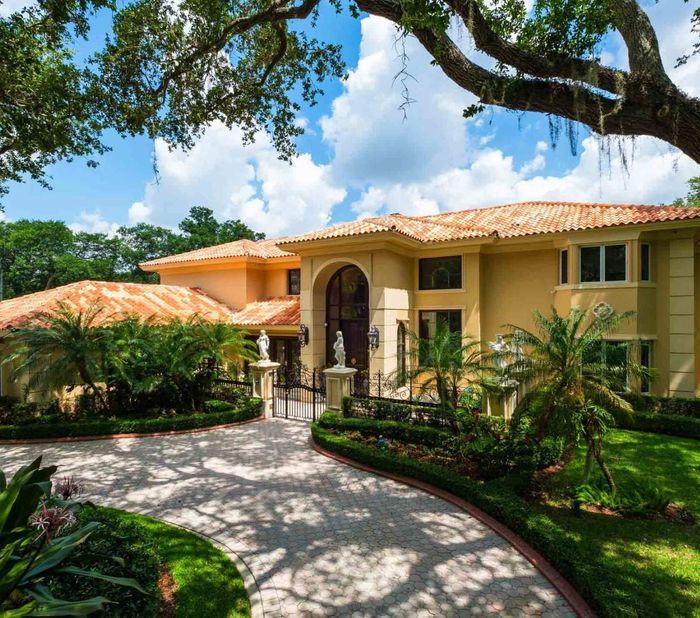 A large house with a driveway leading to it is surrounded by trees and bushes.