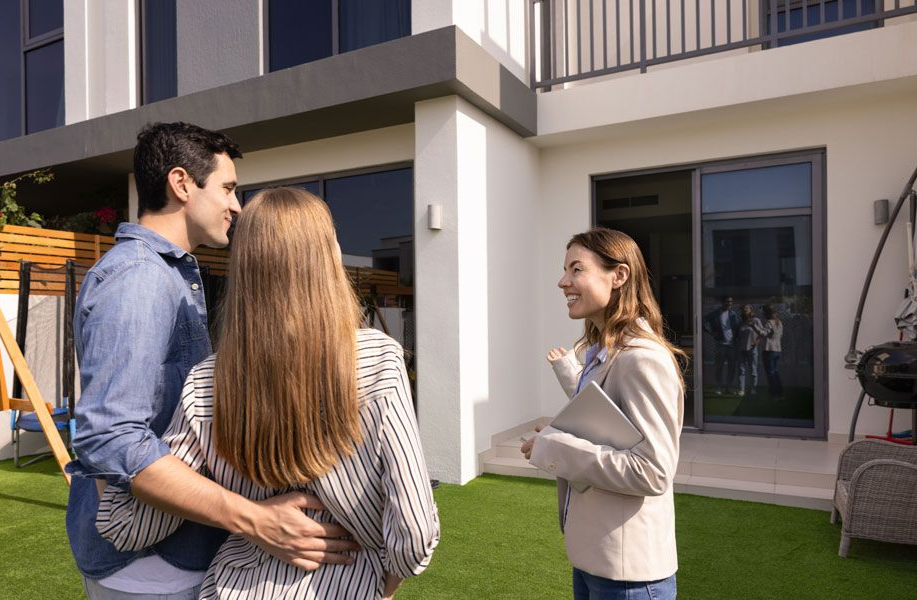 Couple talking with a real estate agent outside a modern house with a green lawn.