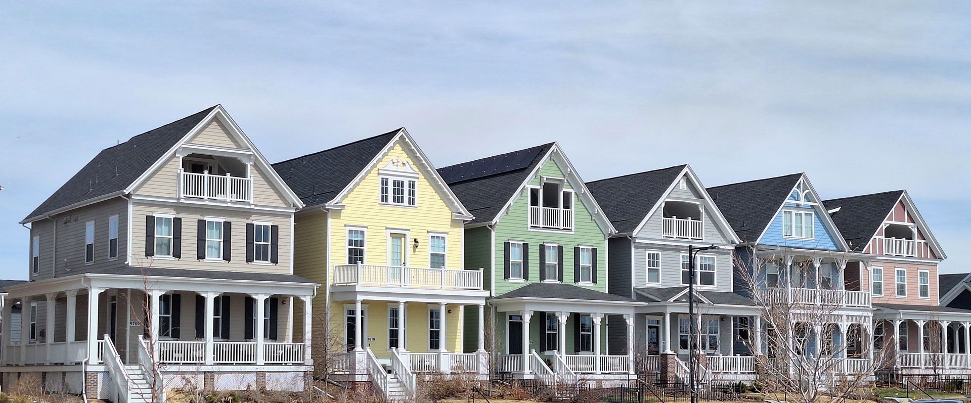 Row of colorful houses with front porches under a blue sky and barren lot.