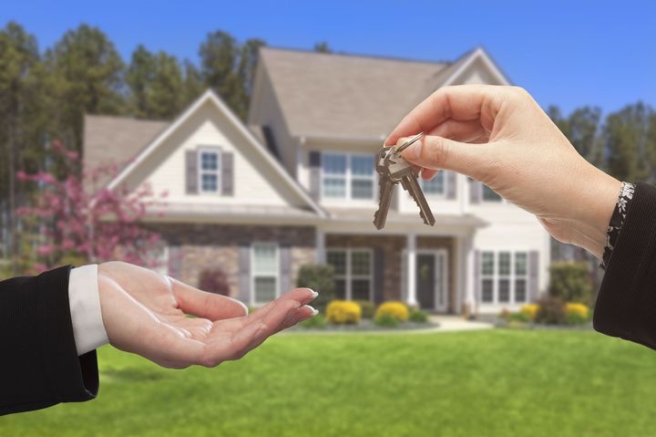 A woman is handing a man a set of keys in front of a house.