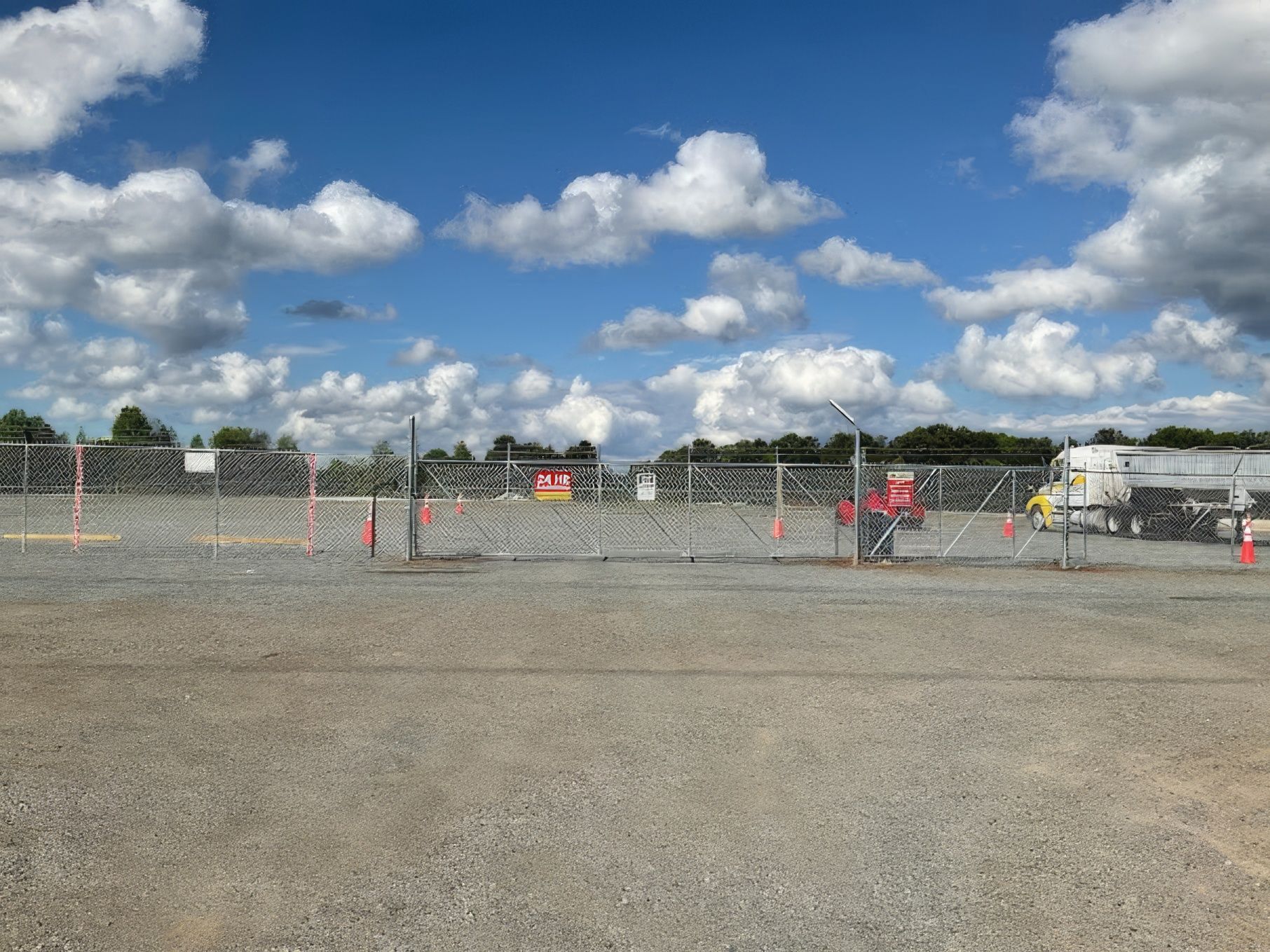 Chain-link fence around a construction site under a blue sky with white clouds