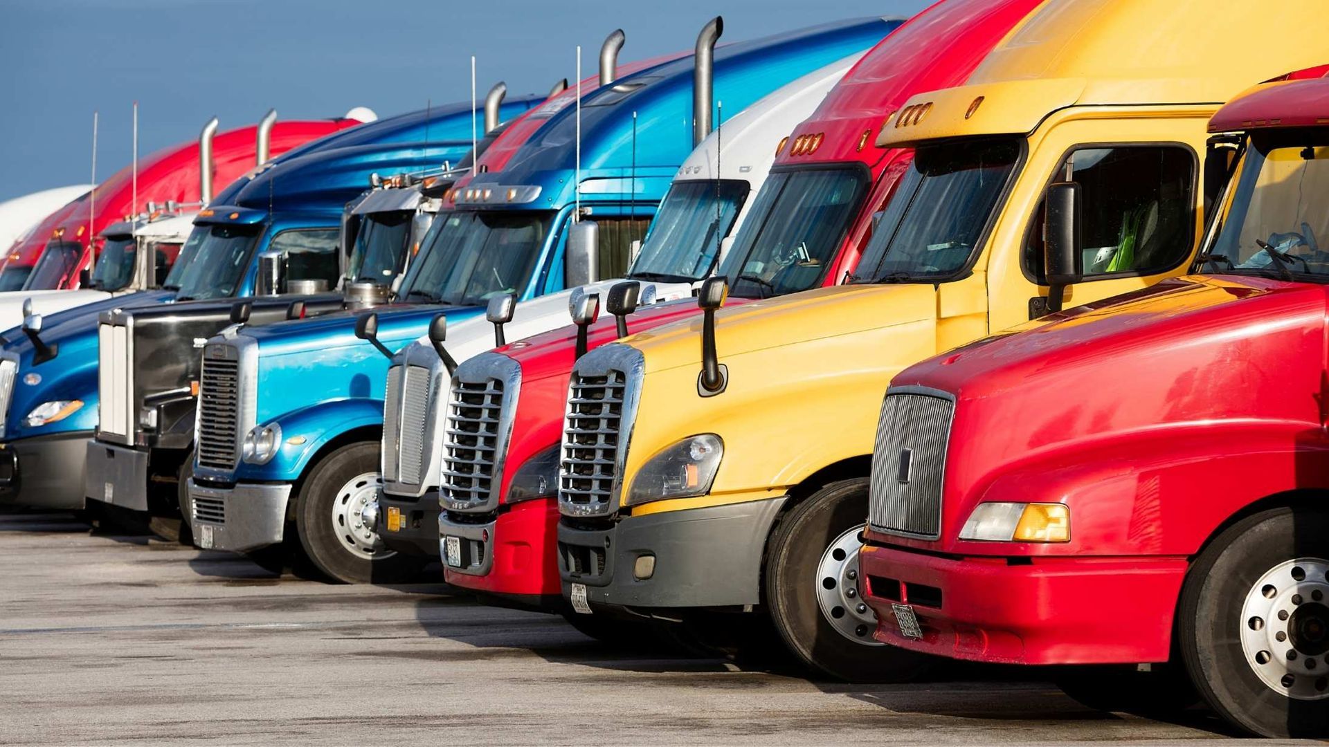 A row of semi-trucks in various colors, including red, yellow, and blue, parked in a lot.