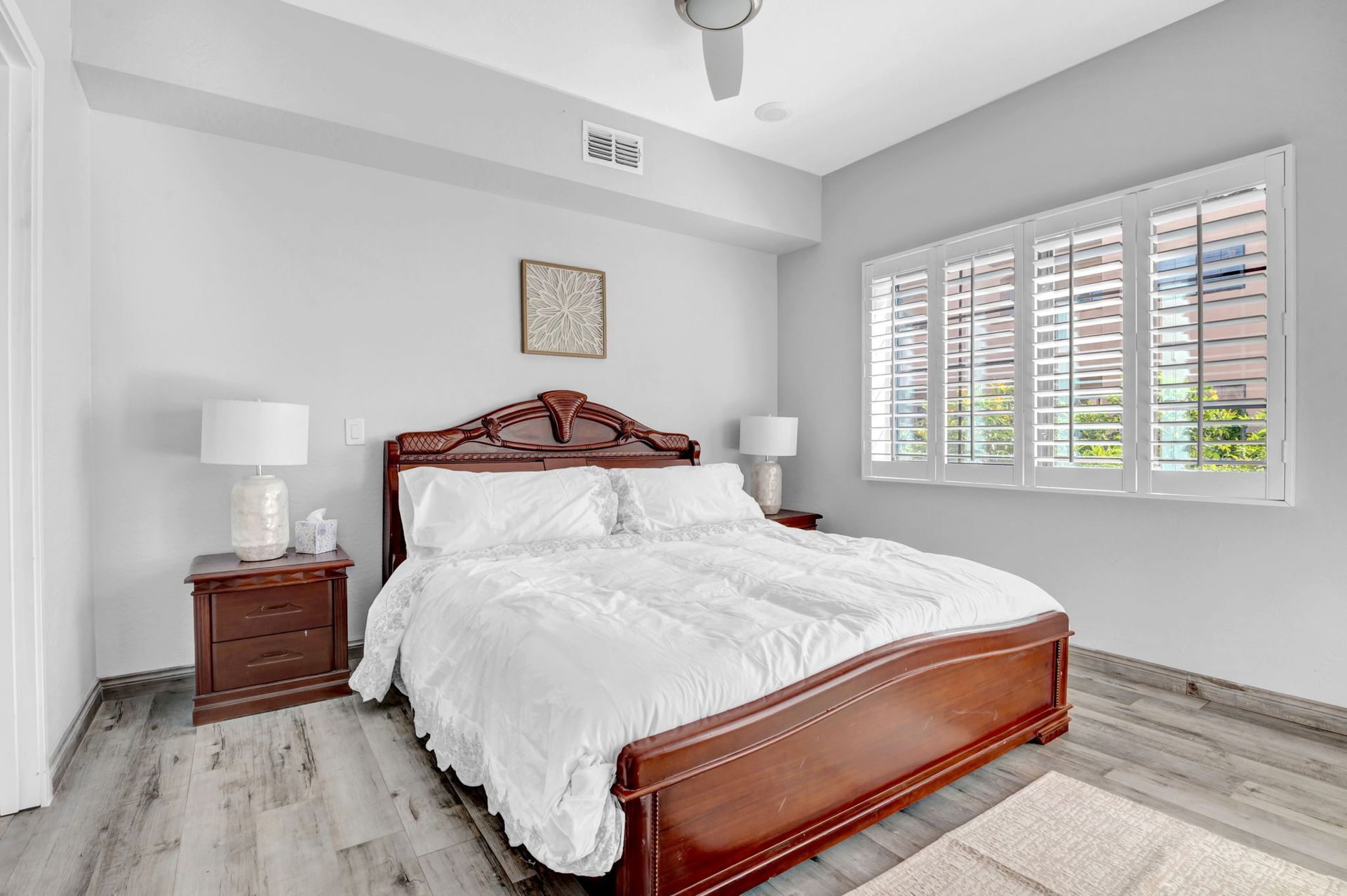 Bedroom with a large bed, nightstands, a window with shutters, and light gray walls.