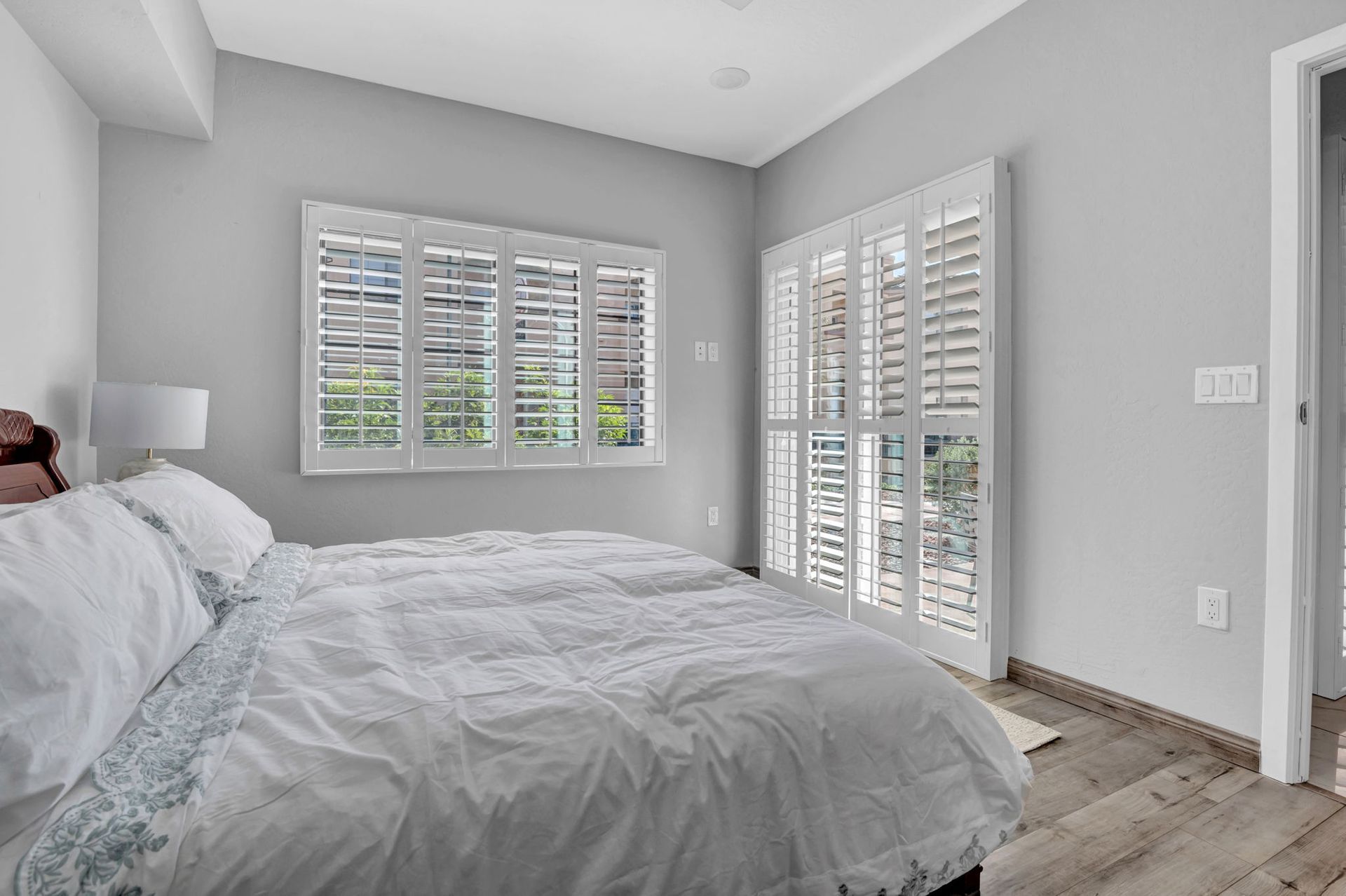 Bedroom with a white bed, shutters on the window and door, and gray walls.