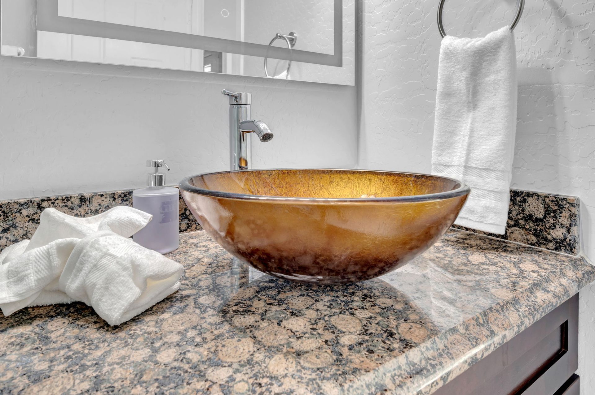Bathroom vanity with brown glass bowl sink on granite countertop, white towel.