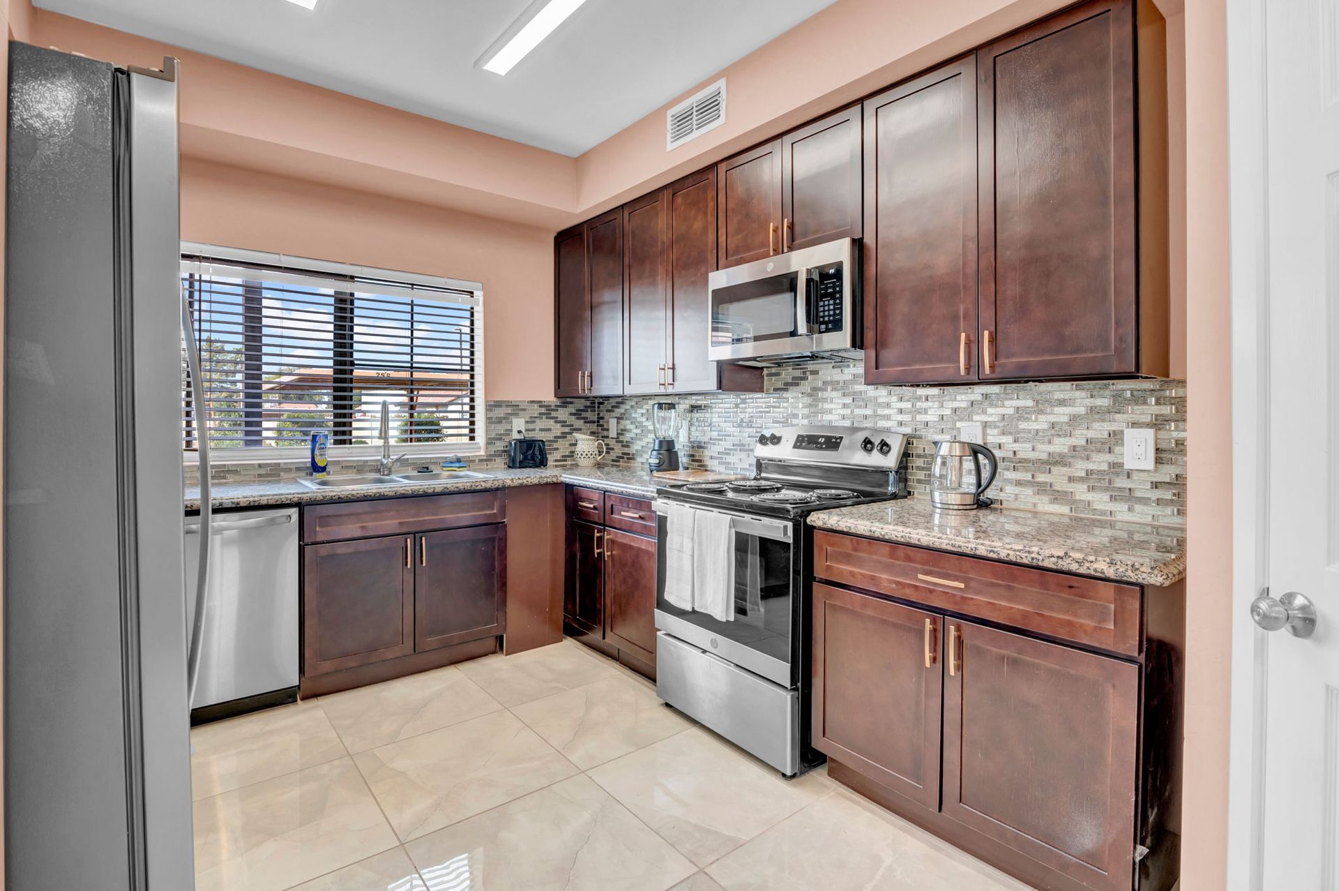 Kitchen with dark wood cabinets, stainless steel appliances, granite countertops, and a window.