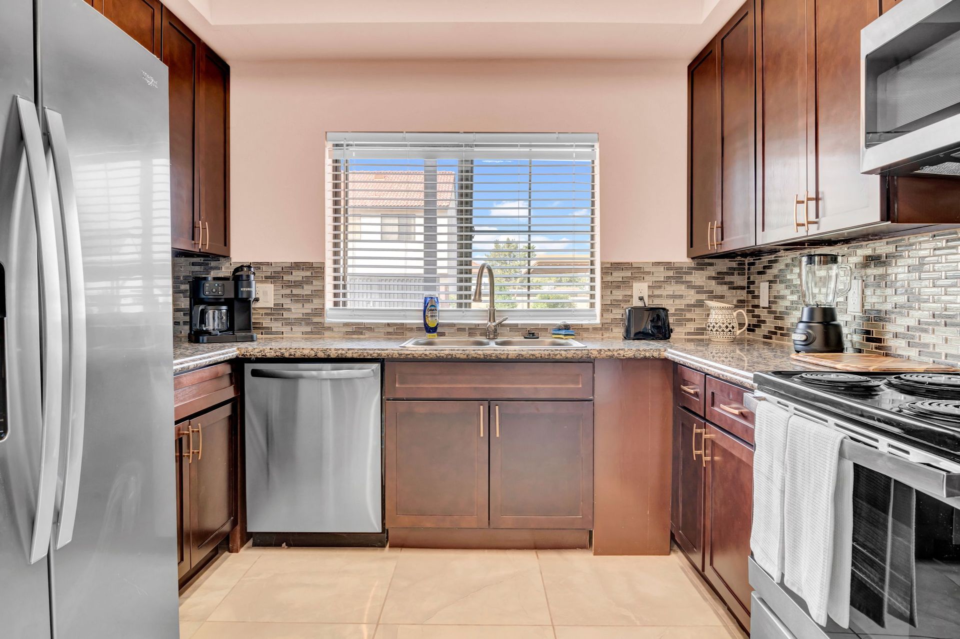 Kitchen with dark brown cabinets, stainless steel appliances, and a window above the sink.