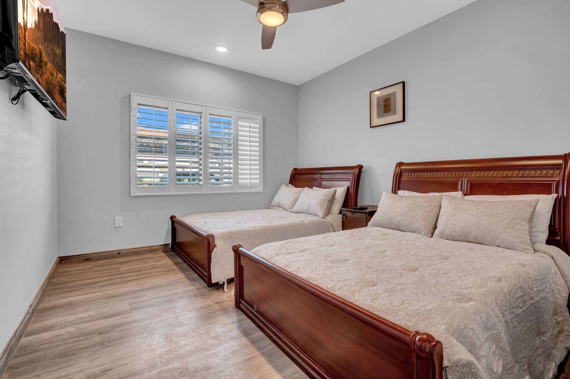 Bedroom with two wooden beds, window with shutters, and wall-mounted television.