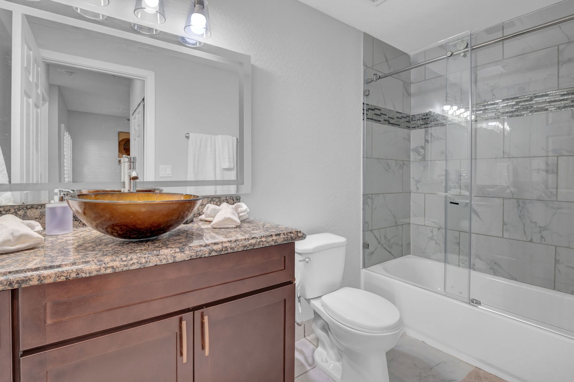 Bathroom with brown vanity, granite countertop, round bronze sink, and tiled shower.