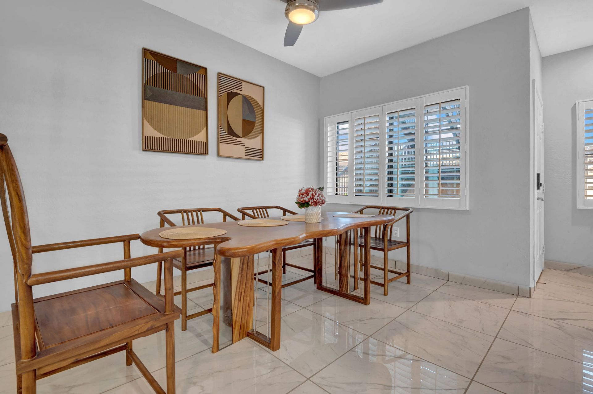 Dining room with wooden table, chairs, art, and window with shutters.