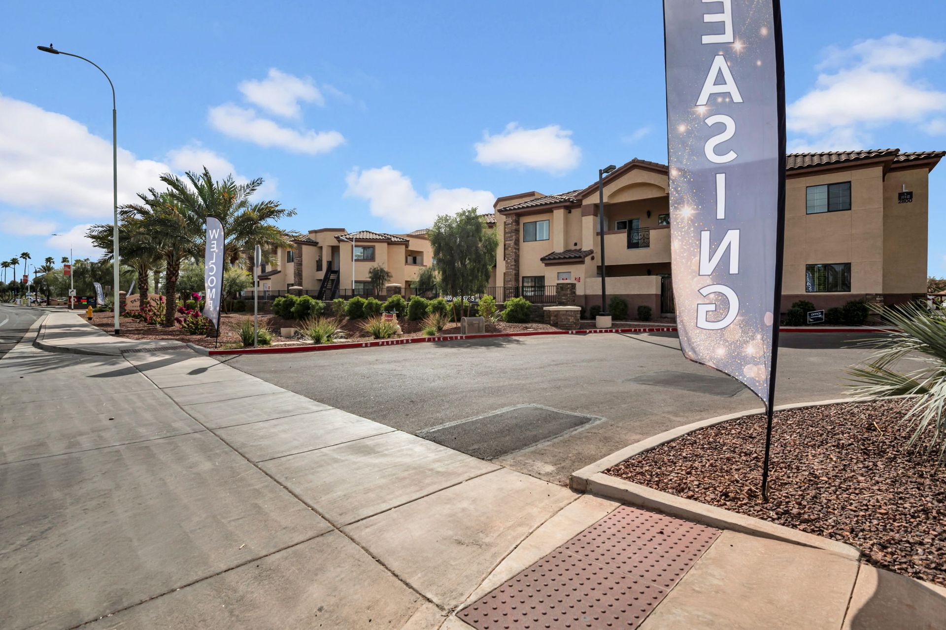 Apartment complex with leasing sign. Buildings are tan, blue sky overhead, palm trees.