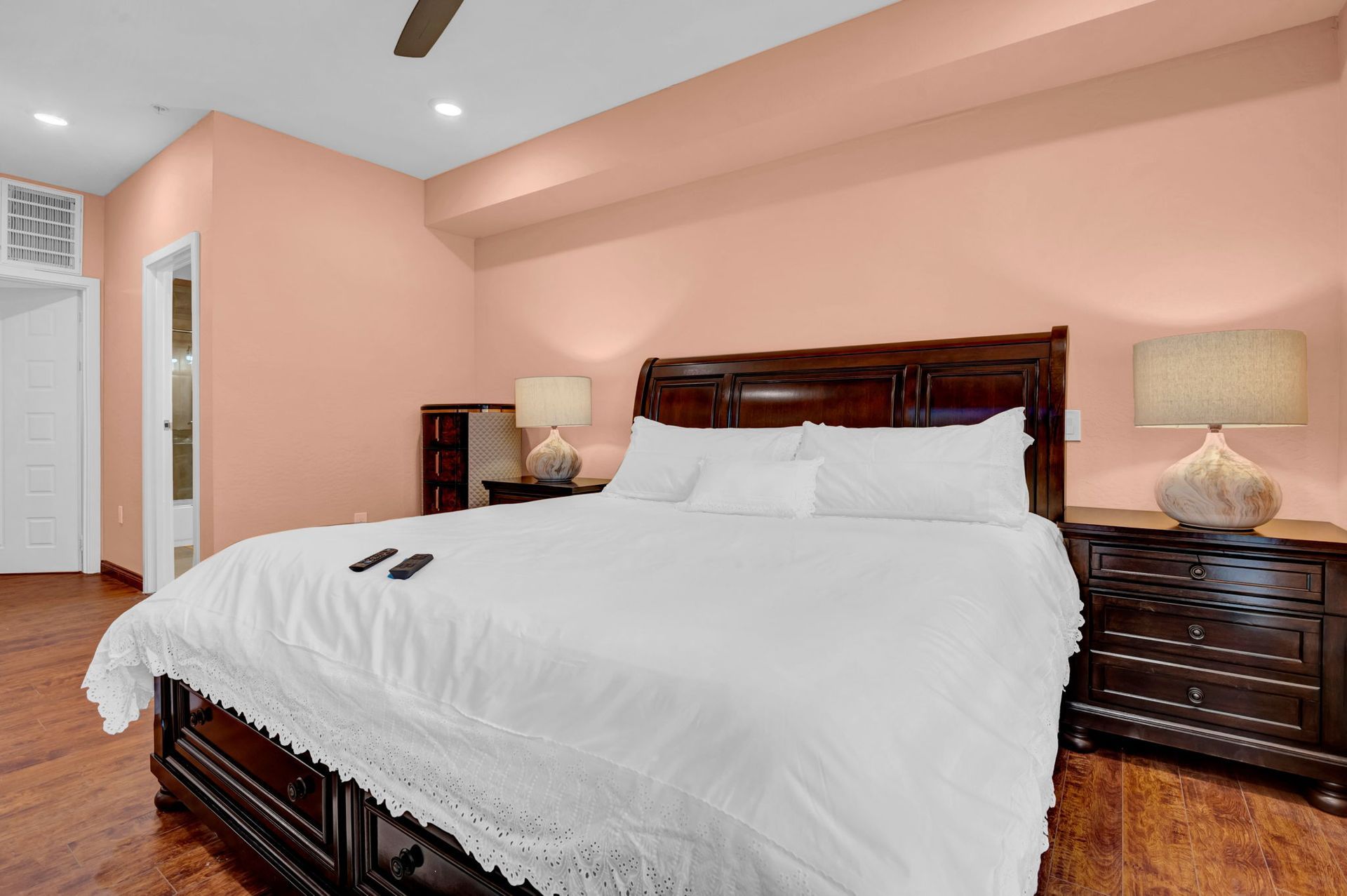 Bedroom with a king-sized bed, dark wood furniture, peach walls, and two bedside lamps.