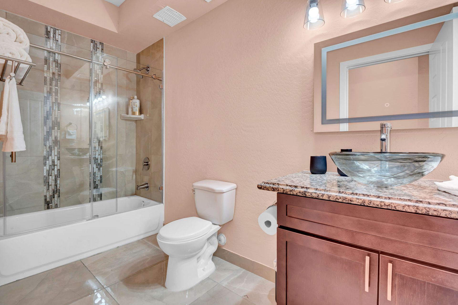 Bathroom with a glass bowl sink, toilet, tub/shower combo, and a pink wall.