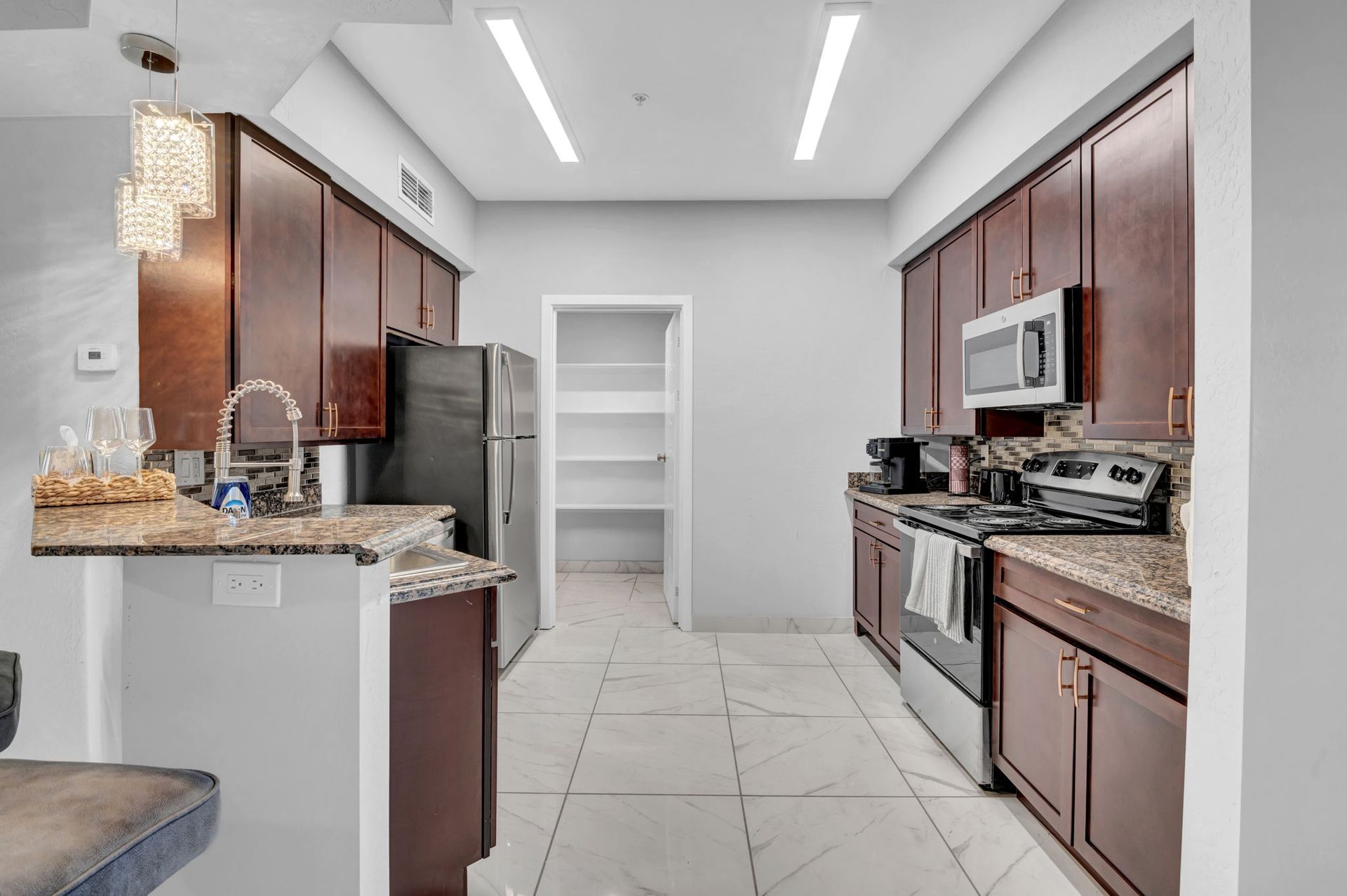 Kitchen with dark brown cabinets, stainless steel appliances, and white tile floor.