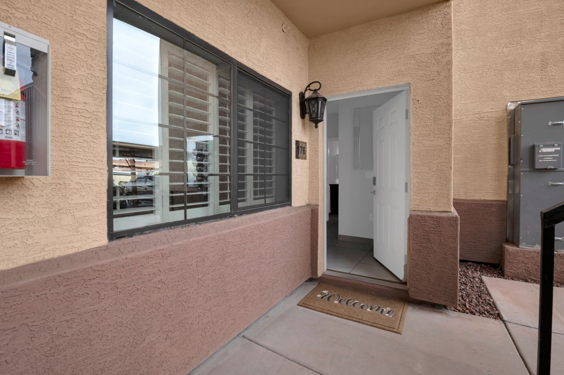 Entryway of a building with open white door, window with metal grate, and beige exterior.