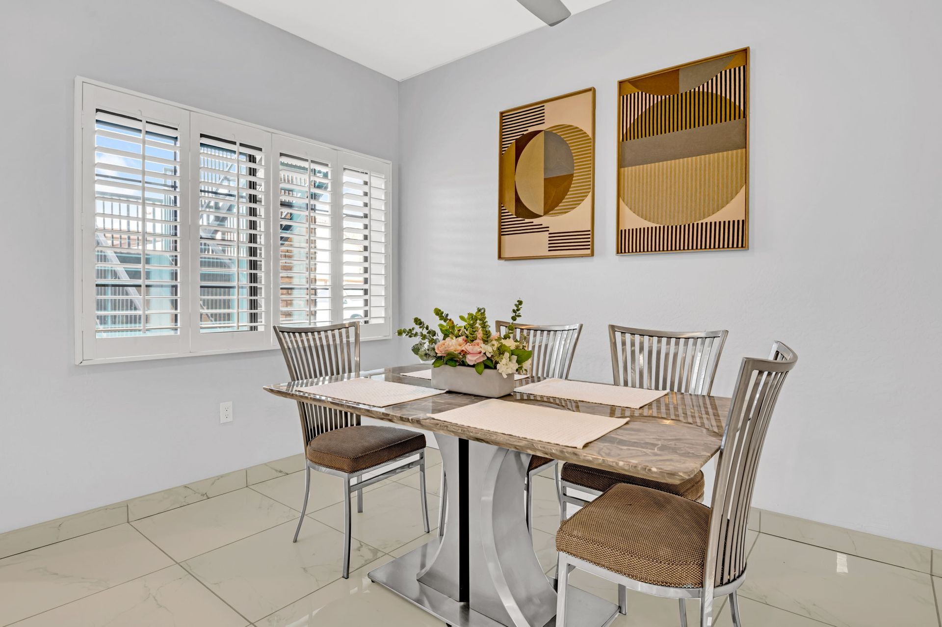 Dining room with table, chairs, art, and window with shutters.