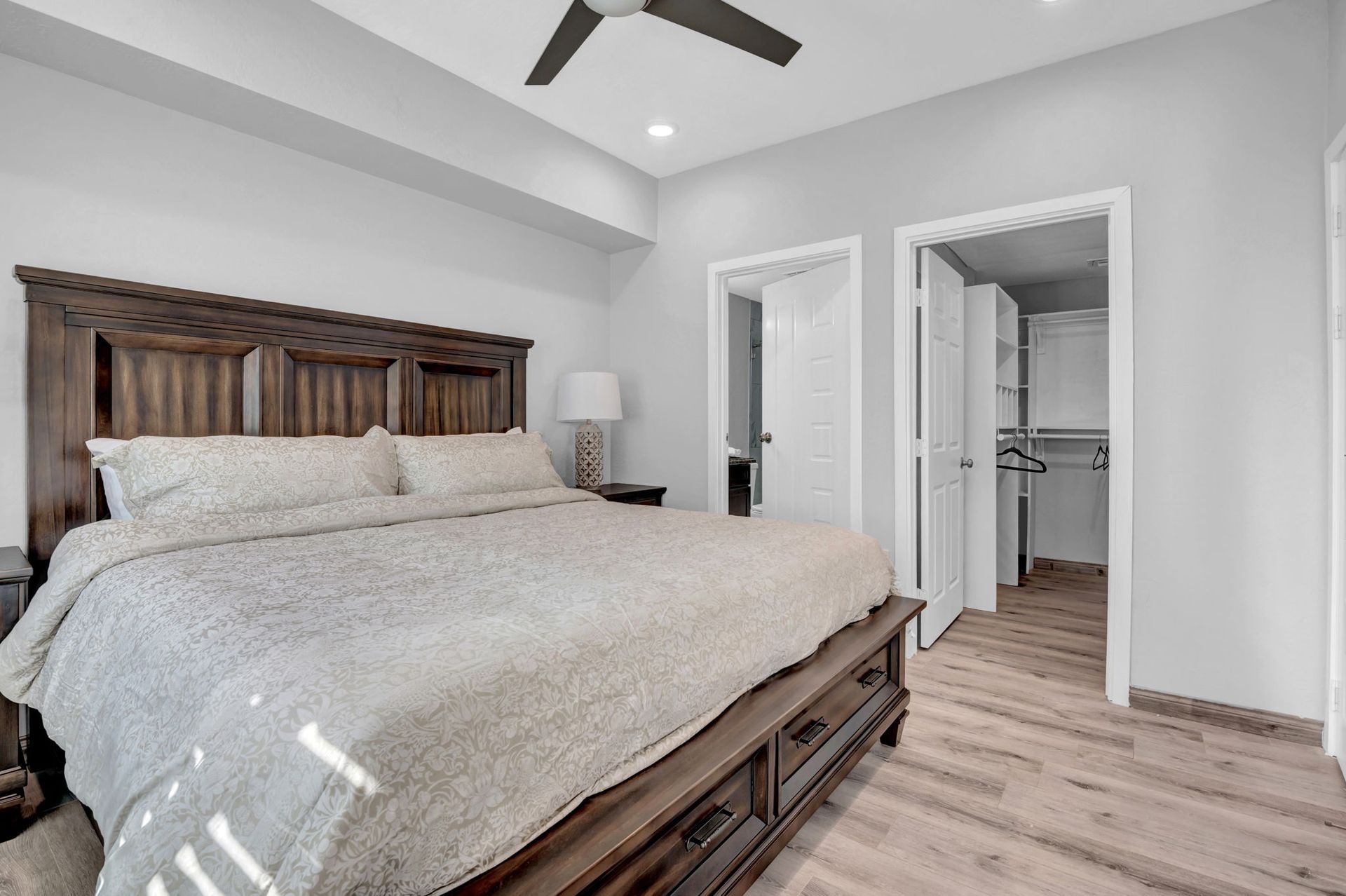 Bedroom with a large wooden bed, two open doors, and a ceiling fan. Light-colored walls and flooring.
