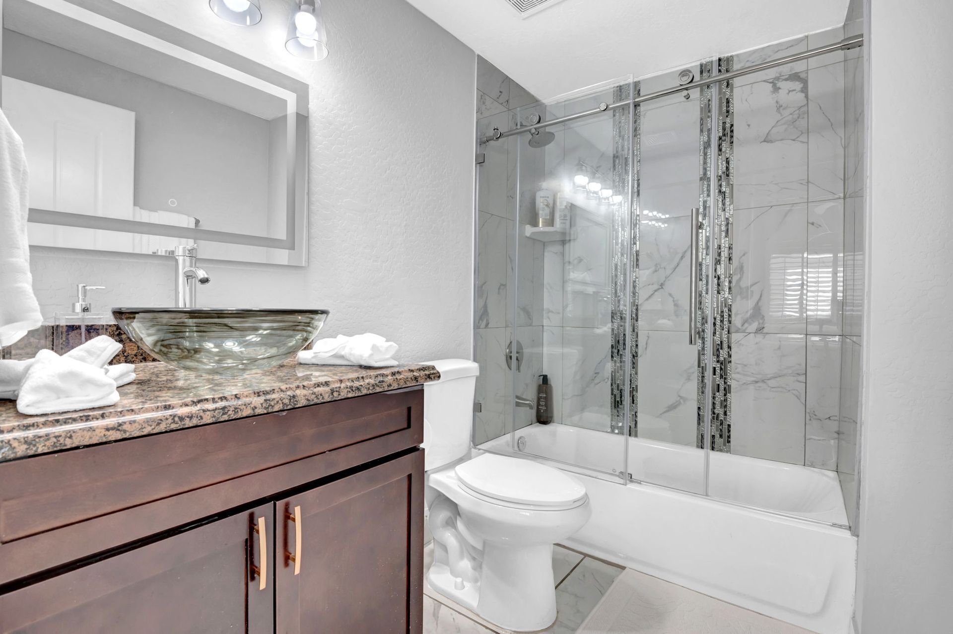 Bathroom with dark brown vanity, glass sink, white toilet, and marble-tiled shower.