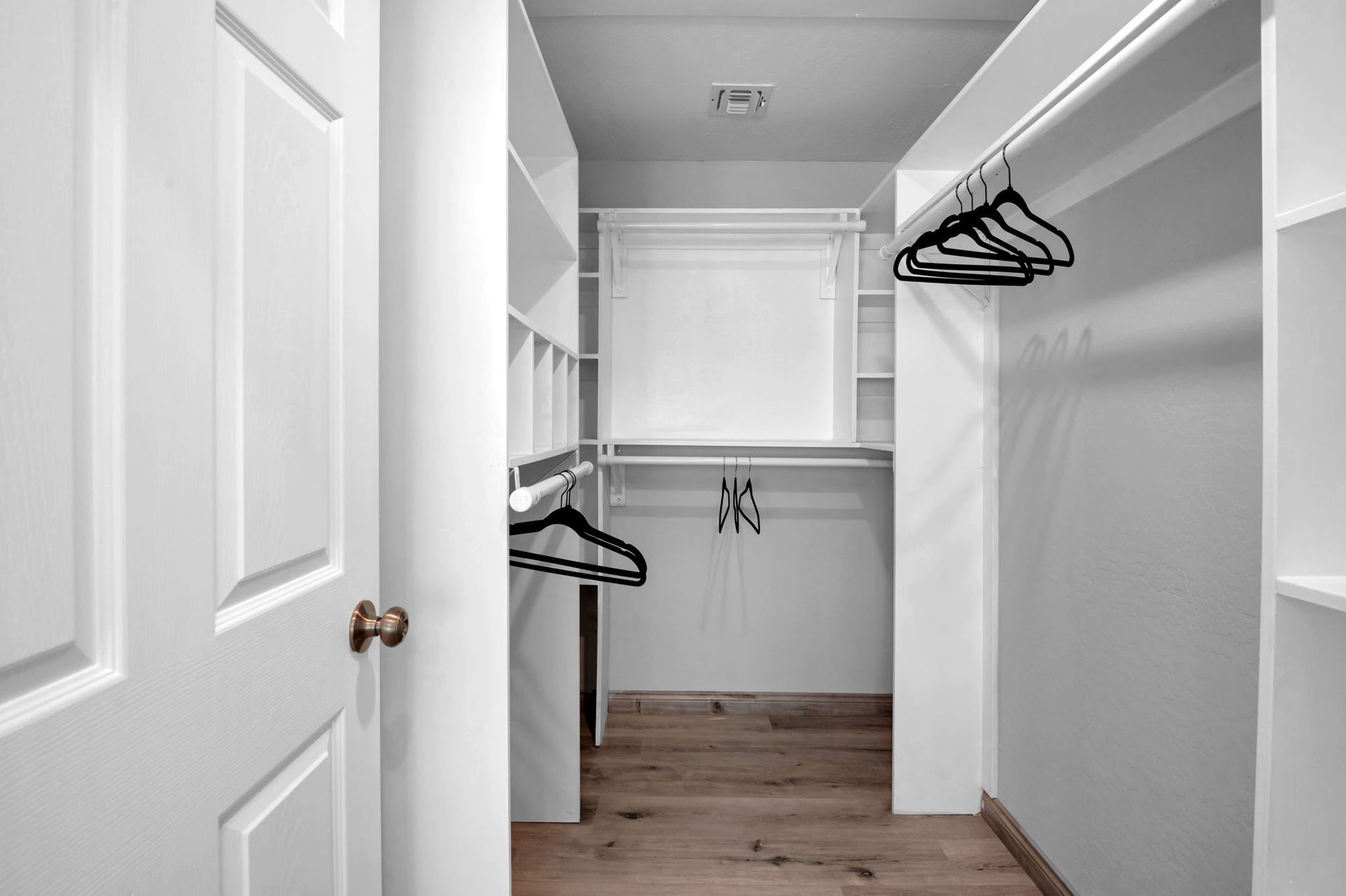 Walk-in closet with white shelves and rods, hanging hangers, and wood flooring.