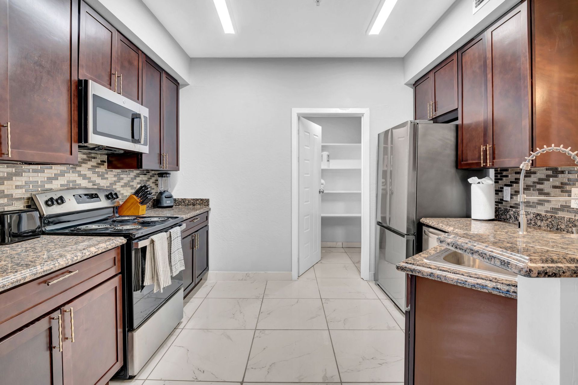 Kitchen with brown cabinets, stainless steel appliances, granite countertops, and a pantry.